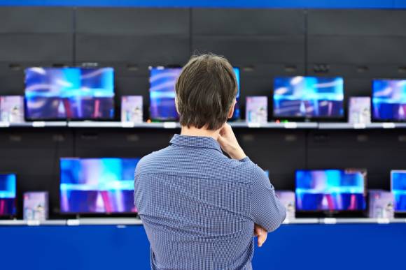 Mann steht vor einer Wand mit Flat-TVs 