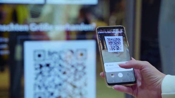 as Smartphone als „Shopping-Fernbedienung“ der Kunden: Am Smart Mirror werden QR-Codes zu Angeboten und Kampagnen eingelesen 