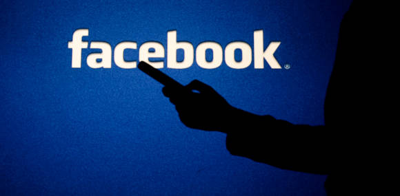 Facebook-Logo und Silhouette einer Hand mit Smartphone 