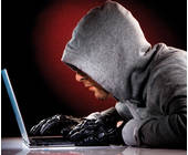 Mann sitzt als Einbrecher getarnt vor einem Laptop